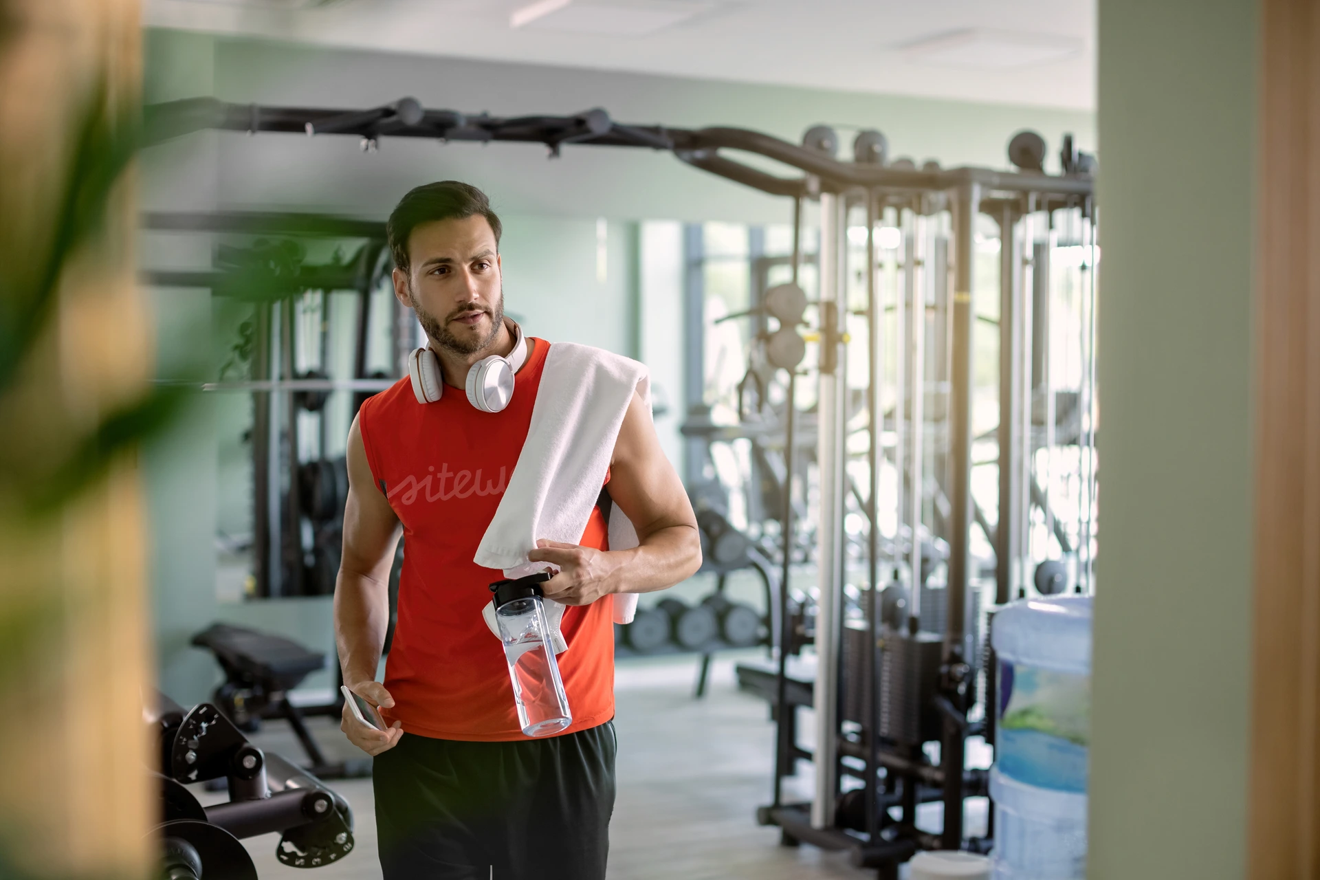 Hombre con toalla en el hombro y botella de agua en el gimnasio