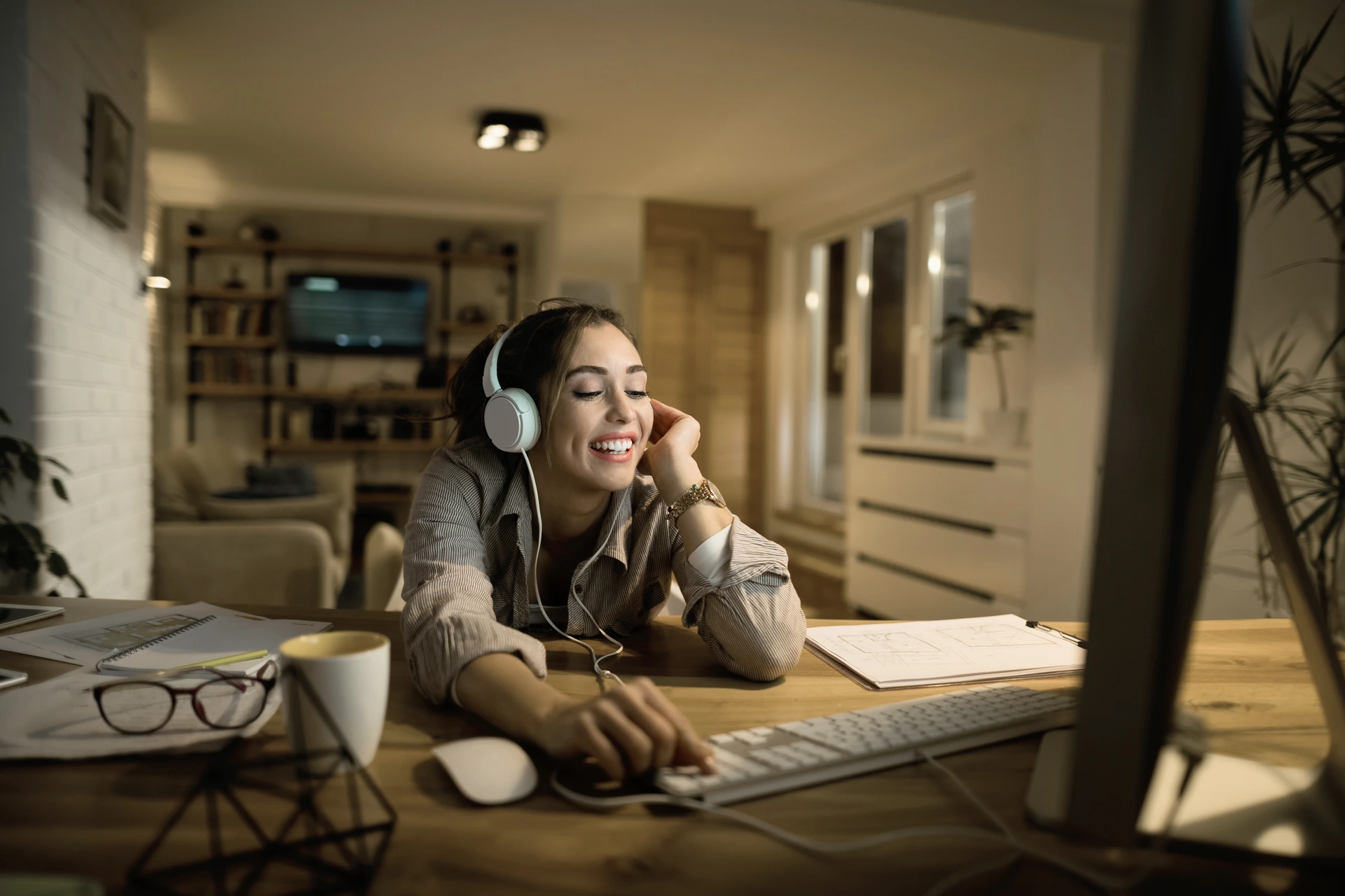 Mujer sonriente con audífonos mientras trabaja en la computadora desde casa