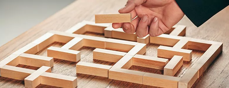Imagem de mão montando labirinto de madeira para representar o planejamento organizacional